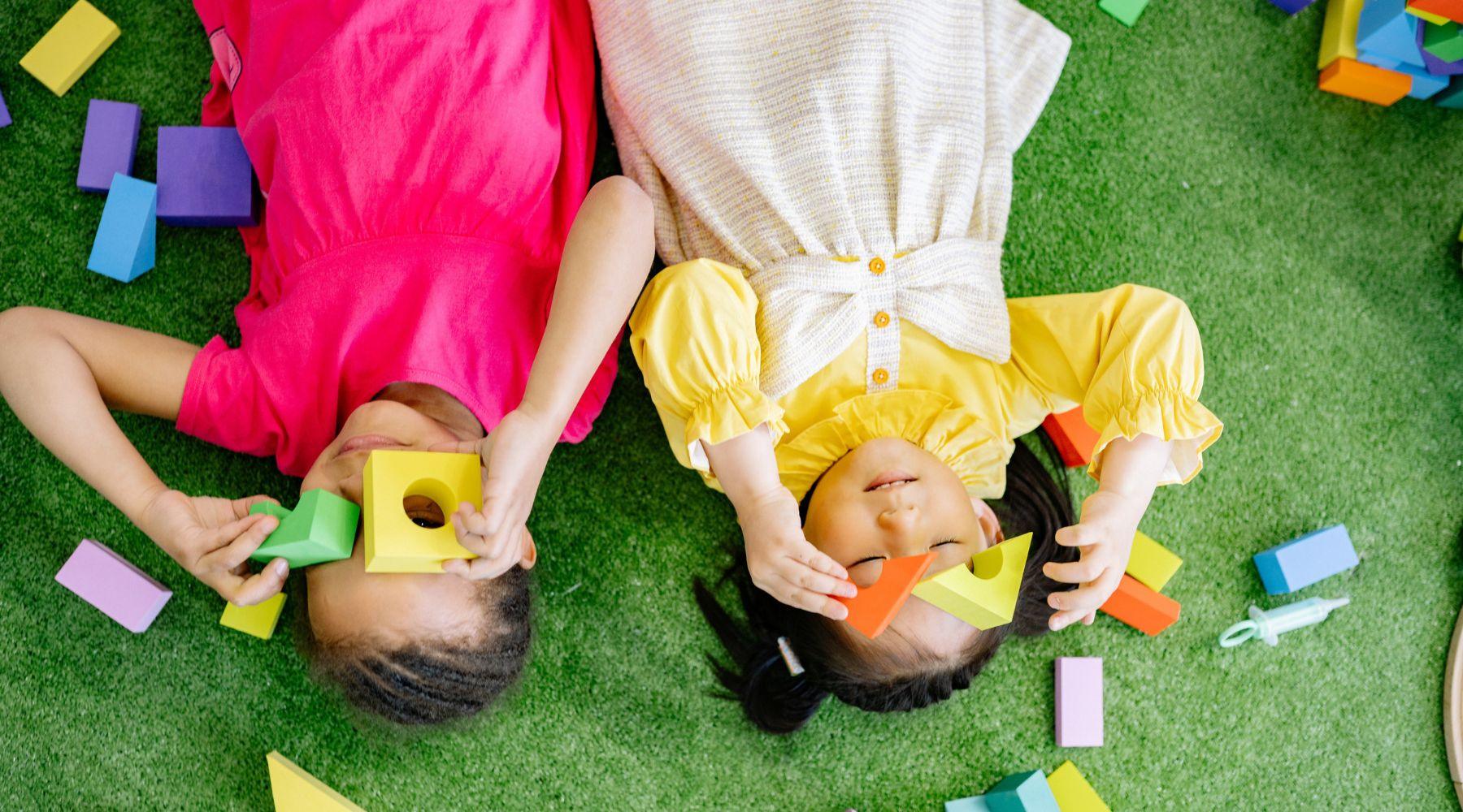 2 kids lying on their back playing with building blocks
